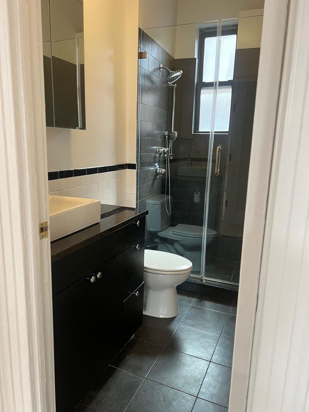 Modern bathroom featuring a glass shower, dark cabinetry, and tiled floor.