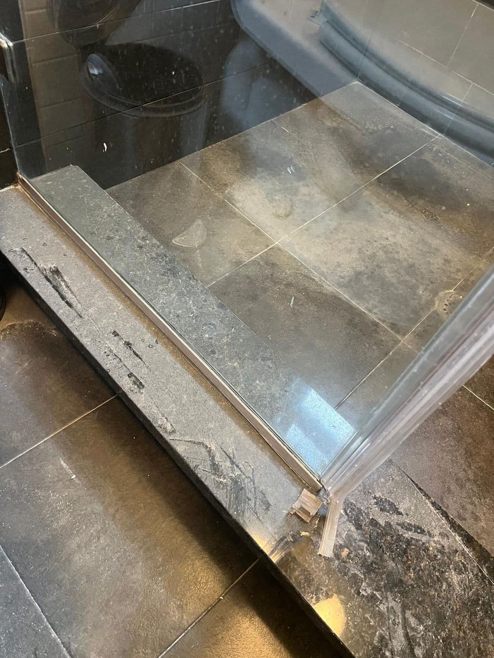 Close-up of a modern glass shower enclosure on dark stone tiles, showcasing clean lines.