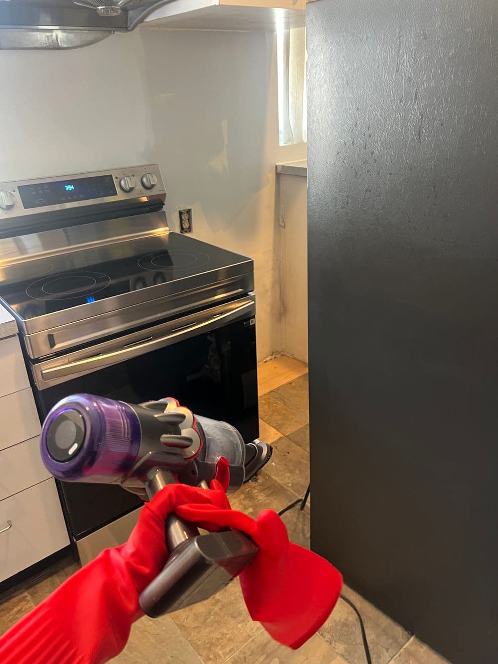 Person in red gloves using a vacuum cleaner in a modern kitchen with stainless steel appliances.