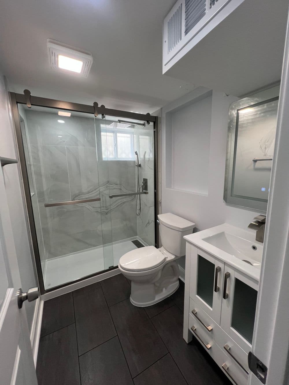 Modern bathroom with walk-in shower, toilet, and vanity with storage. Sleek design and fixtures.
