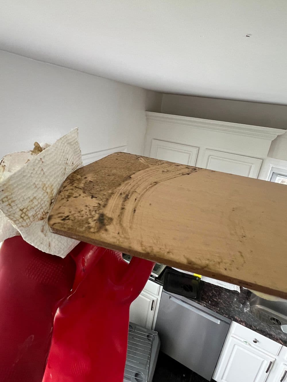 Person cleaning a dirty wooden cutting board with a paper towel in a modern kitchen.
