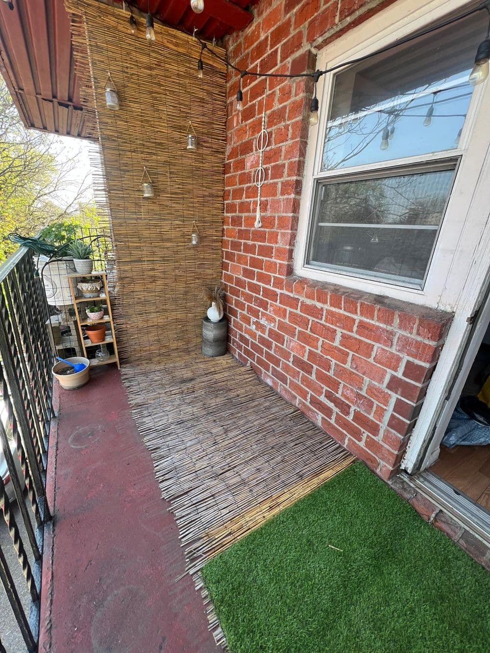 Cozy balcony with bamboo matting, red brick wall, and decorative lights. Perfect for relaxation.