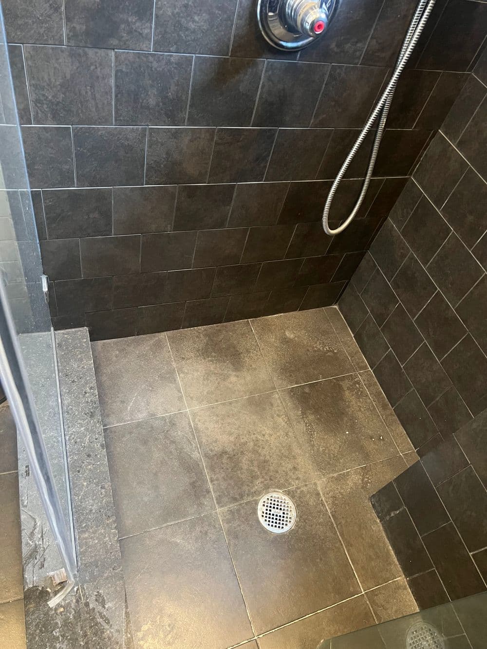 Modern black tiled shower with a chrome showerhead and drainage system. Clean, minimalist design.
