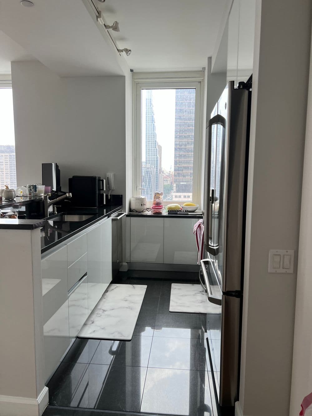 Modern city kitchen with sleek white cabinets, marble mats, and a skyline view.
