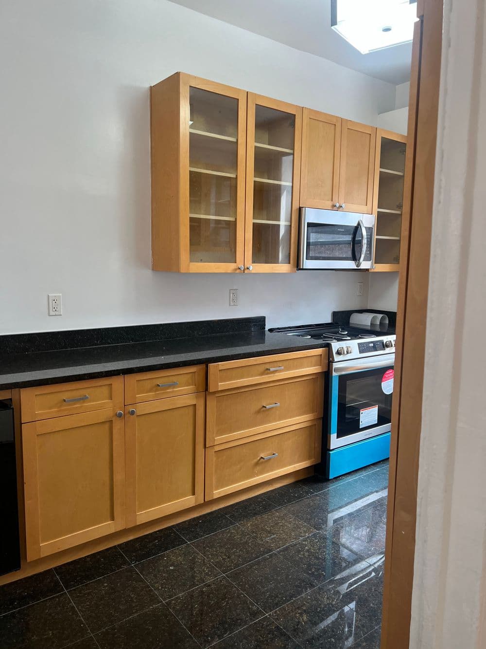 Modern kitchen with wooden cabinets, black countertops, stainless steel stove, and blue accents.